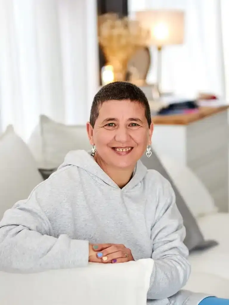Anaís Isarre sentada en un sofá mirando a cámara y sonriendo, mentora experta en recuperar la alegría de vivir.